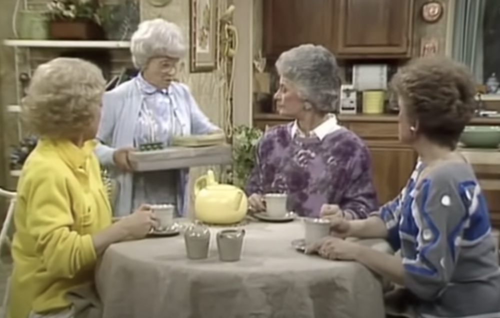 Three women sitting, drinking tea, and one standing